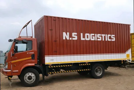 An orange N.S. Logistics container truck with the company name on its side.