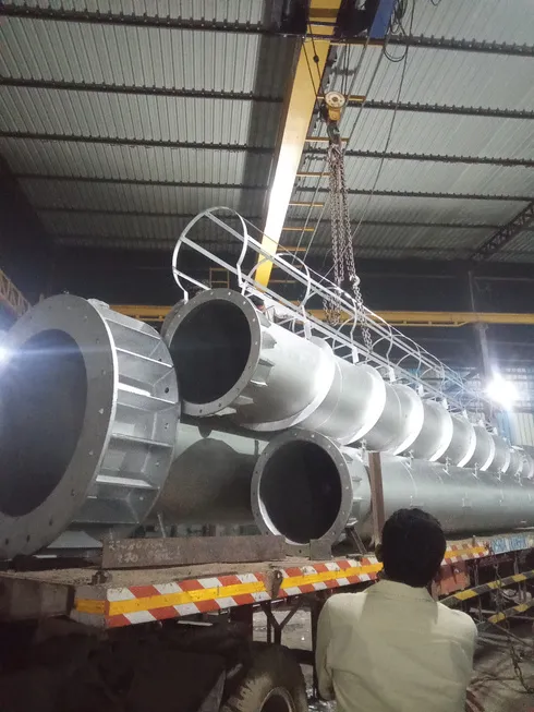 Steel cylindrical sections lifted by an overhead crane onto a trailer inside a factory
