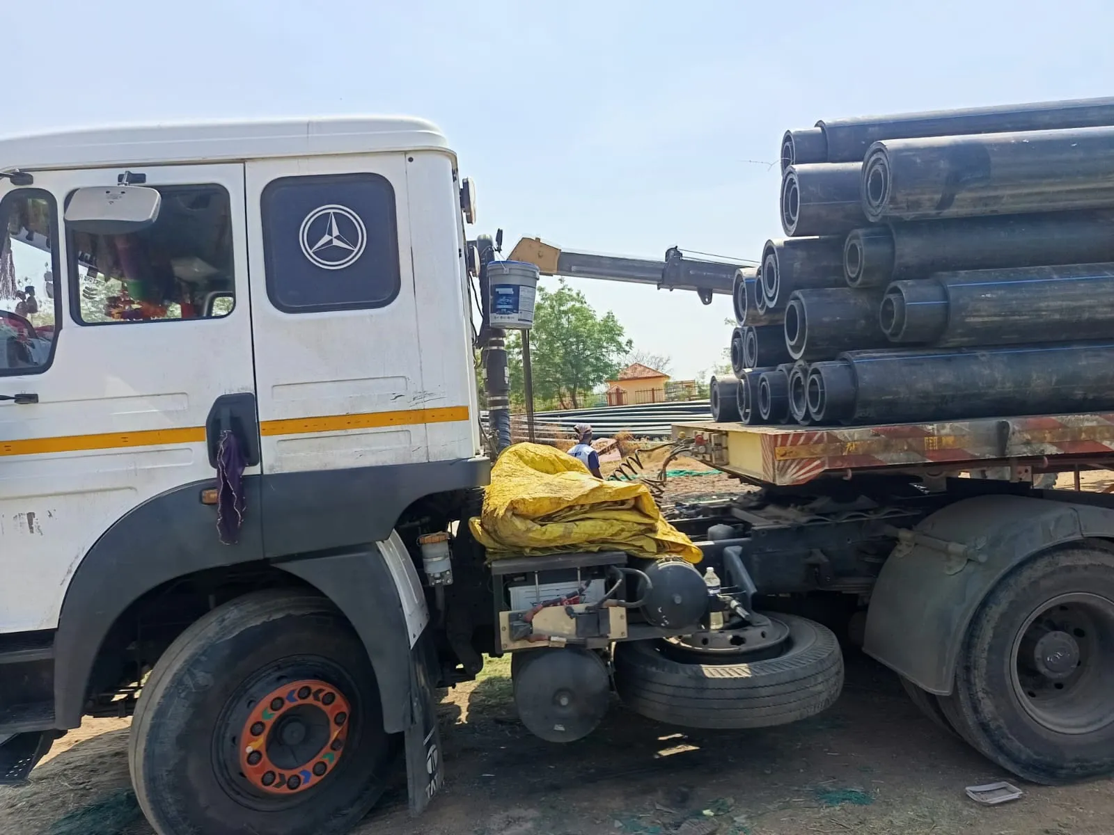 A white truck cab coupled to a trailer stacked with large black pipes, ready for dispatch.