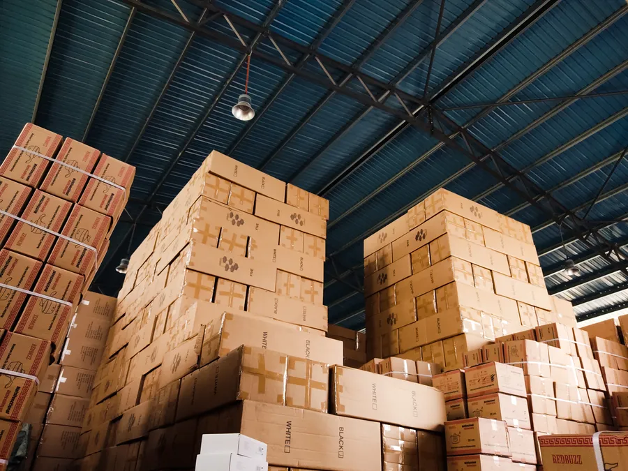 Cartons stacked high in a warehouse under steel roof trusses